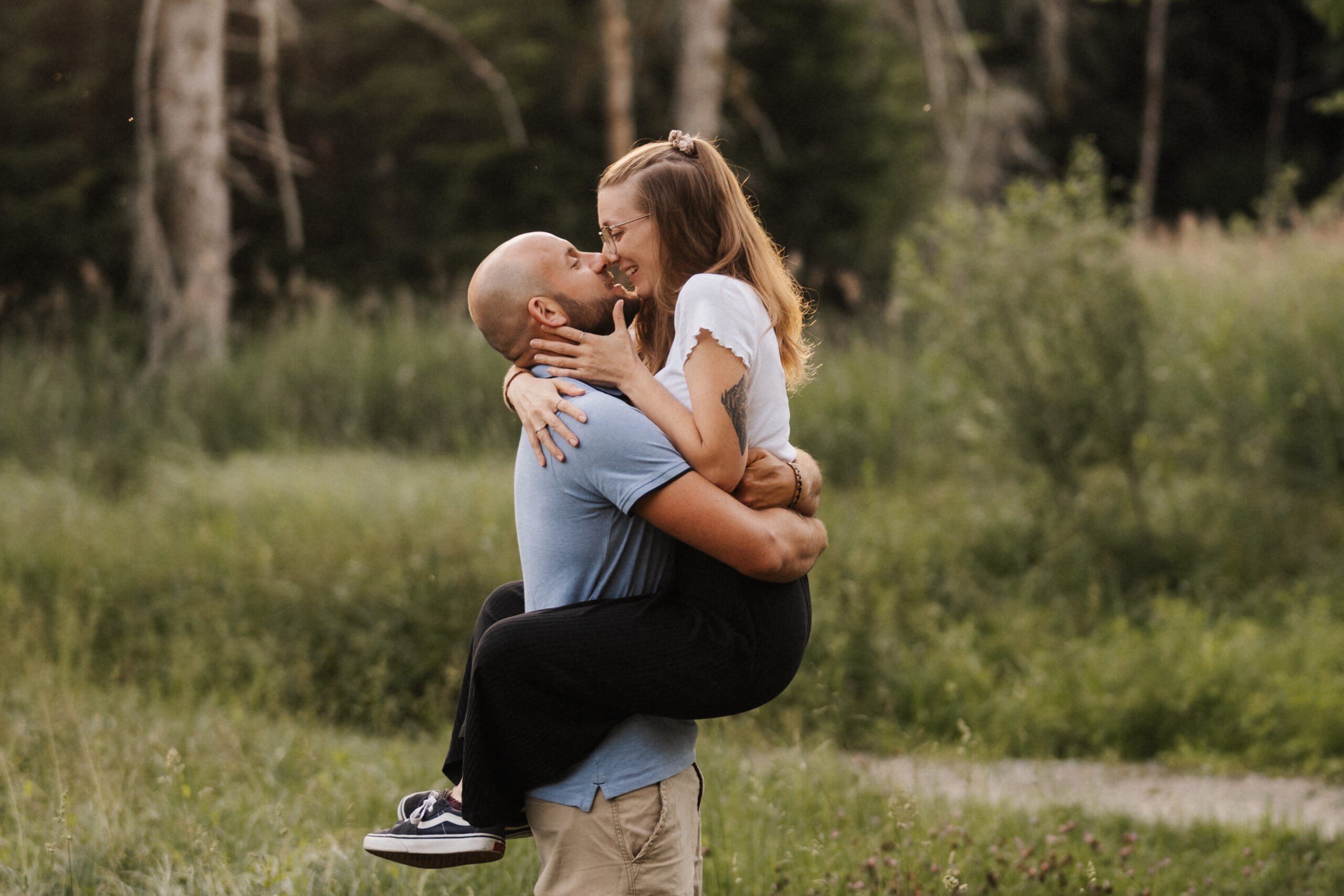 Pre Wedding Shooting in Niederrohrdorf, Mann hebt seine Partnerin auf einer Moorwiese hoch, beide küssen sich im Abendlicht